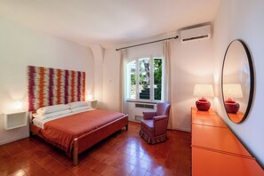 Une chambre à coucher avec un lit, une chaise, une commode, un miroir et une fenêtre avec des rideaux.
