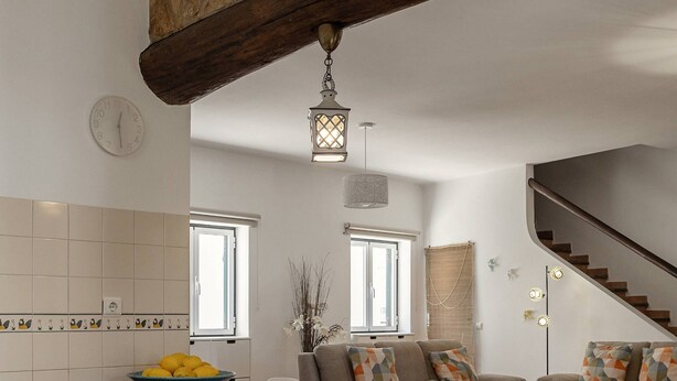 A kitchen with a stone beam, a central island with stools, a staircase, and a dining area. - Quinta Alegria - Rustic Cottage (Alcobaça)