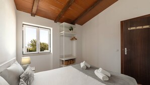 A bedroom with a bed, a window, a shelf with a plant, and a door. - Quinta Alegria - Rustic Cottage (Alcobaça)