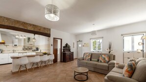 A spacious living area with a kitchen, a dining table, and a sofa with decorative pillows. - Quinta Alegria - Rustic Cottage (Alcobaça)