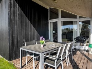 Un patio al aire libre con una mesa, sillas, una parrilla y una pared negra.