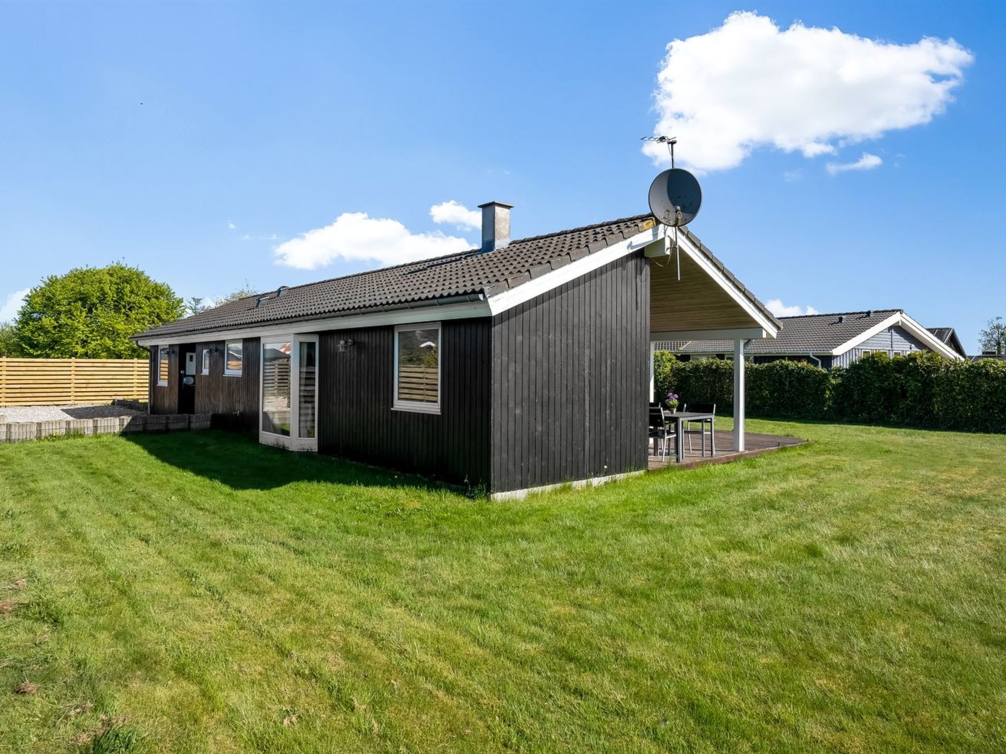 A single-story house with a covered patio, a satellite dish, and a well-maintained lawn.
