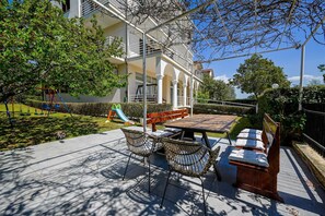 Eine Terrasse mit Tisch und Stühlen, ein Spielbereich für Kinder und ein Gebäude mit Balkonen.