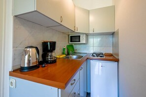 Eine kleine Küche mit Mikrowelle, Kaffeemaschine, Spüle und kleinem Kühlschrank.
