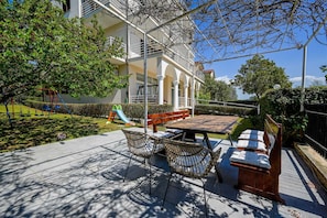 Eine Terrasse mit Tisch und Stühlen, ein Spielbereich für Kinder und ein Gebäude mit Balkonen.