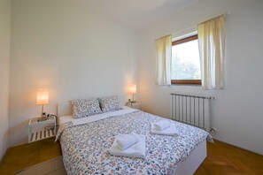 Ein Schlafzimmer mit einem Bett, zwei Nachttischlampen, einem fenster mit Vorhängen und einer Heizung.
