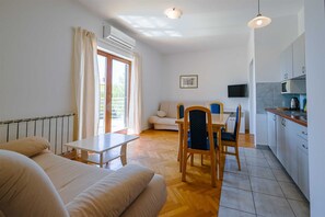 Ein modernes Zimmer mit einem Bett, einem Esstisch mit Stühlen, einer Küchenzeile und einem großen Fenster mit Vorhängen.