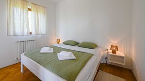 Un letto rifatto con lenzuola verdi e cuscini bianchi, una lampada da comodino e un termosifone.