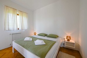 Ein ordentlich bezogenes Bett mit grüner Bettwäsche und weißen Kissen, eine Nachttischlampe und ein Heizkörper.