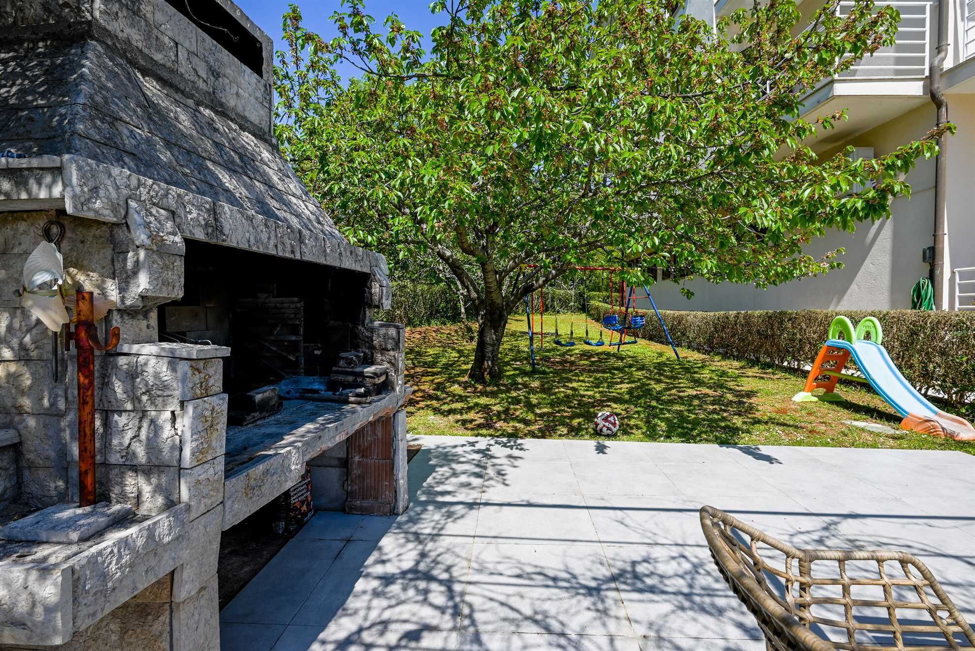 A stone structure with a bench, a tree, and a playground with a slide.