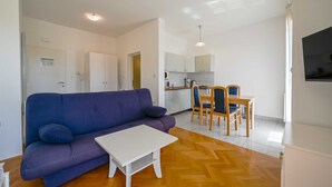 Ein Wohnzimmer mit einer Couch, einem kleinen weißen Tisch und einer Küchenzeile mit Esstisch und Stühlen.