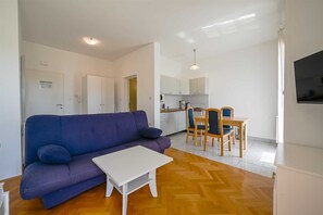 Ein Wohnzimmer mit einer Couch, einem kleinen weißen Tisch und einer Küchenzeile mit Esstisch und Stühlen.