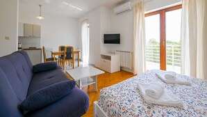 Ein Zimmer mit Bett, einer Couch, einem Fernseher, einem kleinen Tisch und einer Küchenzeile.