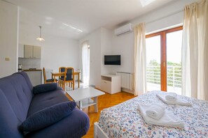 Ein Zimmer mit Bett, einer Couch, einem Fernseher, einem kleinen Tisch und einer Küchenzeile.