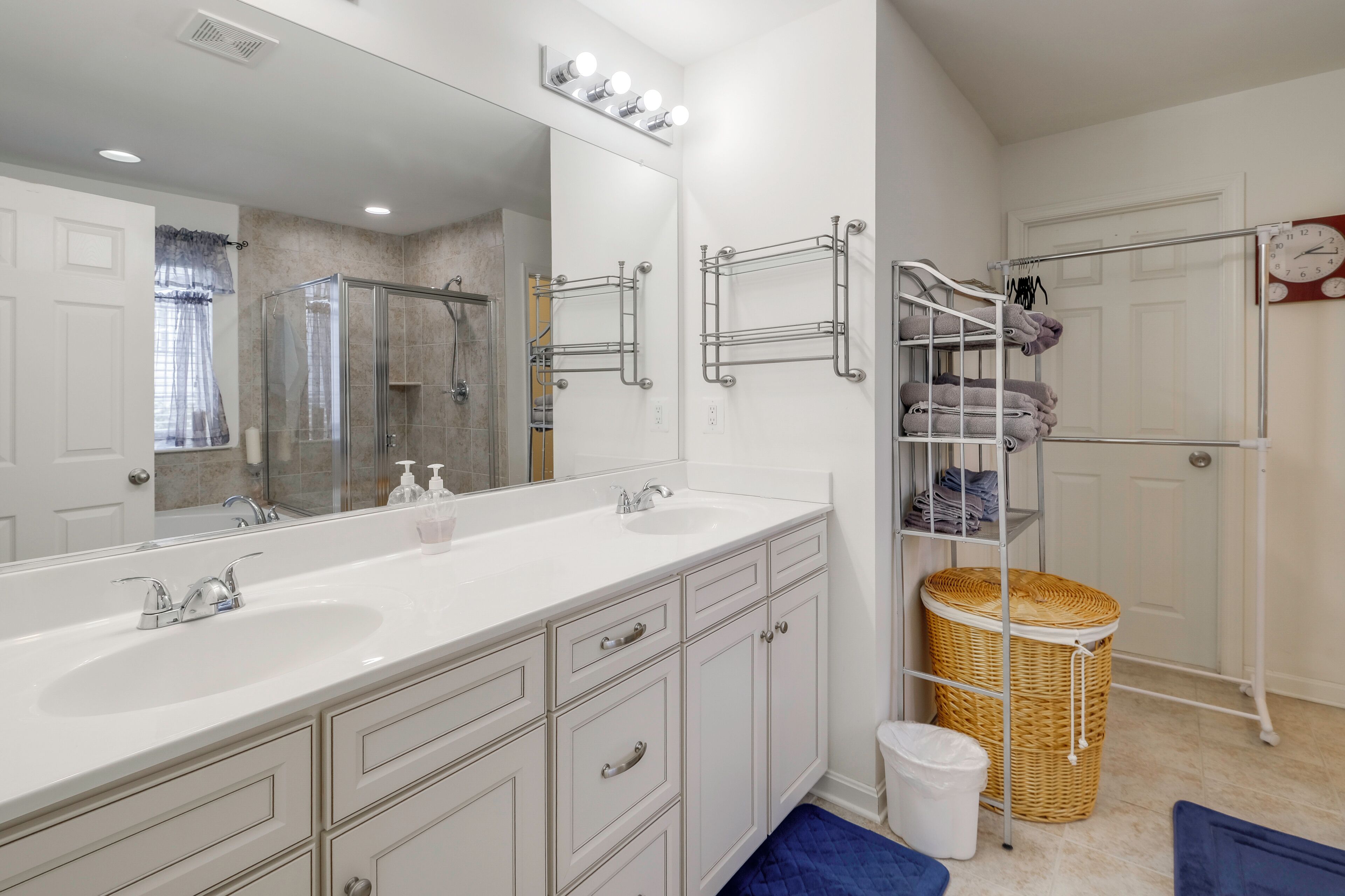 Une salle de bain avec un meuble-lavabo à deux vasques, un grand miroir, une douche et un étagère pour ranger les serviettes.