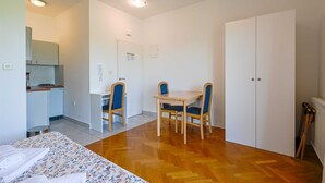 Quarto compacto com cama, pequena cozinha, mesa de jantar com cadeiras e uma porta.