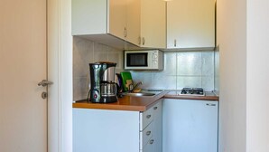 Uma cozinha compacta com armários brancos, micro-ondas, máquina de café e fogão a gás.