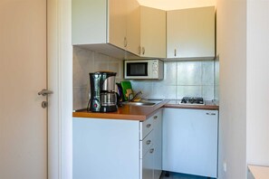 Eine kompakte Küche mit weißen Schränken, einer Mikrowelle, einer Kaffeemaschine und einem Gaskochfeld.