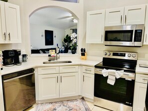 Una cocina moderna con armarios blancos, un microondas de acero inoxidable, un horno negro y una cafetera.