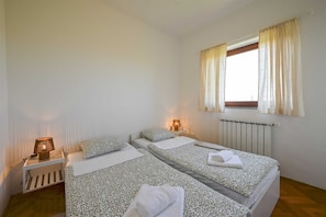 Ein Schlafzimmer mit zwei Betten, einem Heizkörper, einem Fenster mit Vorhängen und Nachttischlampen.
