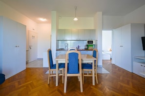 Eine moderne Küche mit weißen Schränken, einem Esstisch mit Stühlen und einem Fernseher auf einem Schrank.
