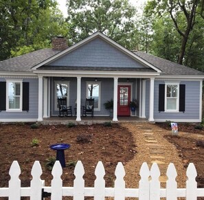A two-story house with a front porch, a red door, and a small garden area.