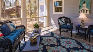 A covered porch with wicker furniture, a patterned rug, and a view of trees and a building.
