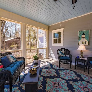 A covered porch with wicker furniture, a patterned rug, and a view of trees and a building. - Book your last minute stay in September-perfect location to enjoy sunset views! (Mentone)