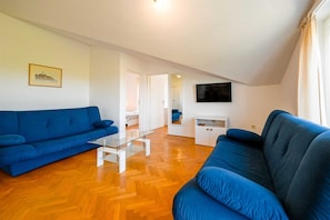 Ein Wohnzimmer mit zwei blauen Sofas, einem Glastisch, einer weißen TV-Konsole und Holzböden.