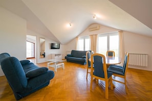 Ein Loft-Wohnzimmer mit einer Couch, Sesseln, einem Fernseher und einem Esstisch.