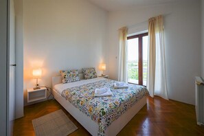 Ein Schlafzimmer mit einem Bett, zwei Nachttischlampen, einem Fenster mit Vorhängen, einer Heizung und einem Holzboden.