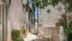 Une rue étroite bordée d’immeubles, avec un mur de pierre et un petit espace extérieur aménagé avec une table et des chaises.