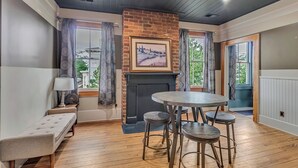 A cozy room with a fireplace, a round table with stools, a bench, and a view of the outdoors. - Charming 2BR w/ Porch • Historic Stay Near Forsyth Park (Savannah)
