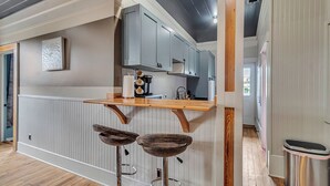 A kitchen with grey cabinets, a wooden countertop, and two woven stools. - Charming 2BR w/ Porch • Historic Stay Near Forsyth Park (Savannah)