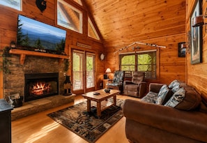 A cozy cabin interior with a fireplace, wooden walls, a television, and a comfortable seating area. - Mountain Escape w/ Hot Tub & Game Room (Sevierville)