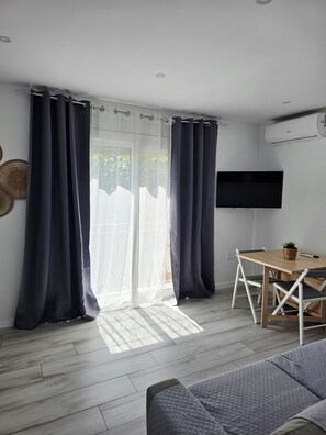 Ein Zimmer mit Glastür, Flachbildfernseher, Holztisch und einer Couch.