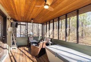 Eine Holzdielen-Terrasse mit Deckenventilator, Korbmöbeln und Blick auf den Wald.