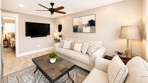Ein Wohnzimmer mit Sofa, Couchtisch, Fernseher, Deckenventilator, Kunstwerken und einer Lampe.