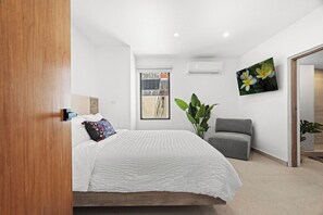 A modern bedroom with a bed, a grey armchair, a large plant, and a painting on the wall. - Villa Bali: Private Pool | 2 Min Walk to Beach (San Juan)