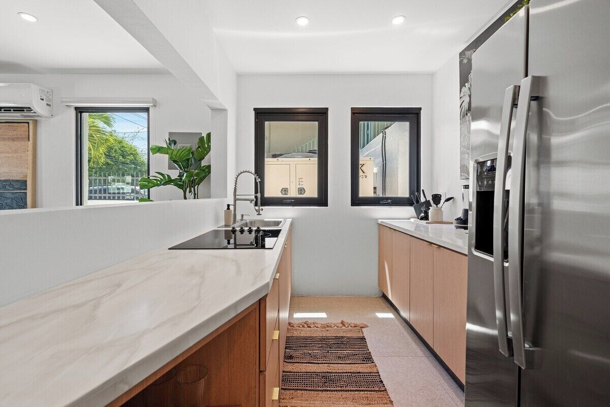A modern kitchen with a stainless steel refrigerator, a sink, and a window overlooking a residential area.