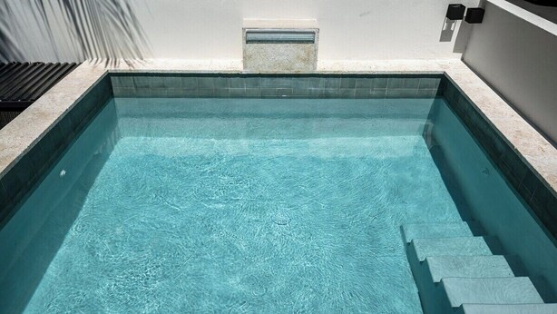 Ein rechteckiger Swimmingpool mit klarem Wasser, umgeben von einer weißen Mauer und einer Fliesenbordüre.