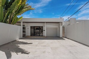A modern building with a flat roof, a garage door, and a paved entrance area. - Villa Tropical: Private Pool | 2 Min Walk to Beach (San Juan)