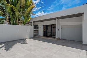 A modern building with a garage, a covered entrance, and a paved patio area. - Villa Tropical: Private Pool | 2 Min Walk to Beach (San Juan)