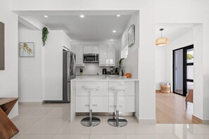A modern kitchen with white cabinetry, stainless steel appliances, and a central island with stools. - Villa Tropical: Private Pool | 2 Min Walk to Beach (San Juan)