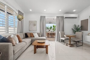 A modern living room with a sofa, coffee table, and dining area. - Villa Tropical: Private Pool | 2 Min Walk to Beach (San Juan)