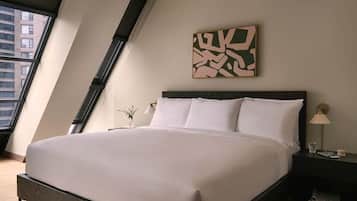 Un dormitorio moderno con una cama grande, una mesita de noche, un cuadro abstracto en la pared y una ventana con vistas a edificios.
