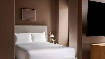 Une chambre d’hôtel avec un lit, un téléviseur fixé au mur, une table de chevet avec une lampe et un tableau encadré accroché au mur.
