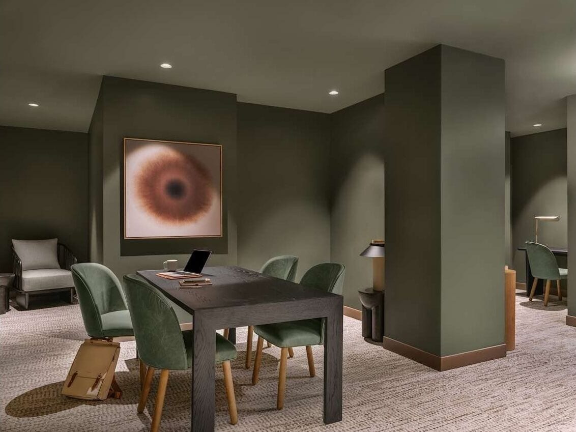 A modern conference room with a dark table, green chairs, a large abstract painting, and a carpeted floor.