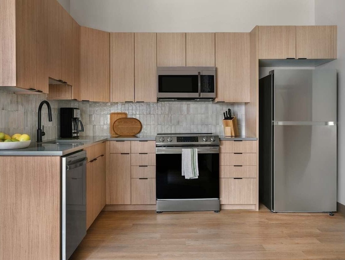Een moderne keuken met houten kastjes, een roestvrijstalen koelkast, een magnetron, een oven en een vaatwasser.
