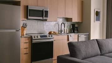 Una cocina moderna con microondas, estufa y horno, un comedor con mesa y sillas, y un sofá gris en primer plano.